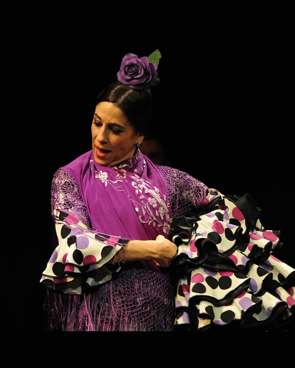 Marisa Adame, bailaora flamenca con traje morado, flor en el pelo y volantes de lunares durante una actuación.